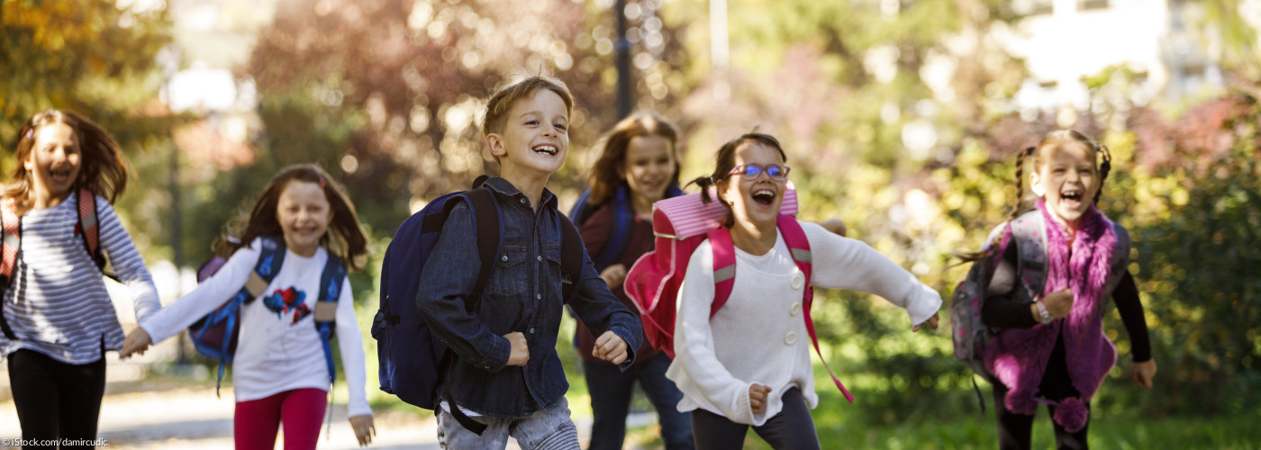 Grundschulkinder mit Schulranzen rennen einen Weg entlang